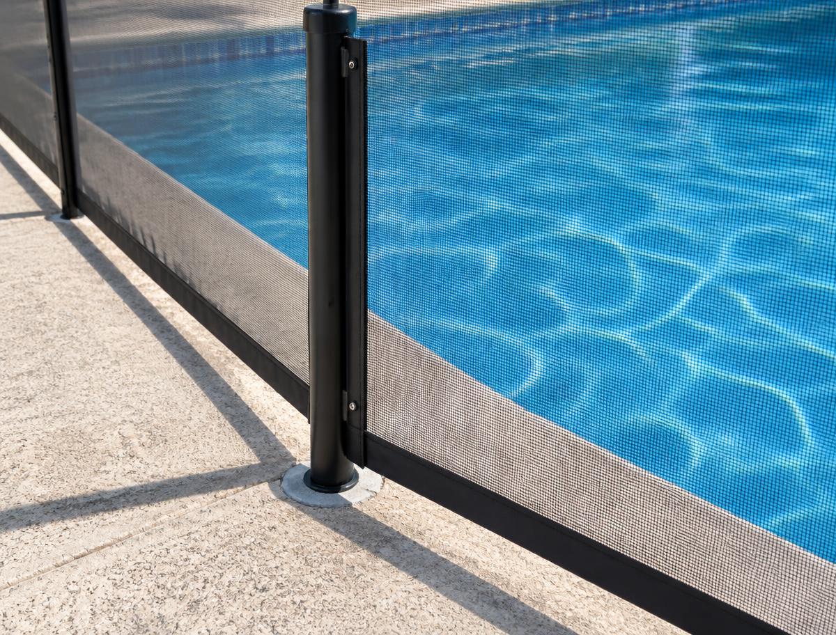 Close-up of mesh pool fence panel and pole on a pool deck